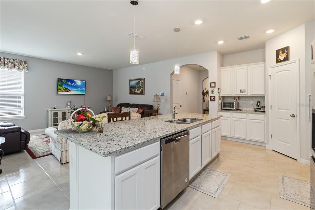 A kitchen with white cabinets and granite countertops overlooks an open-concept living room — 2916 HOODED CRANE COVE, ST CLOUD, FL