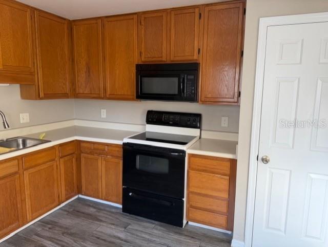 A kitchen features wood cabinets, a black stove, a microwave, and grey wood-look flooring — 8209 OLYMPIA COURT UNIT 8209, LONGWOOD, FL