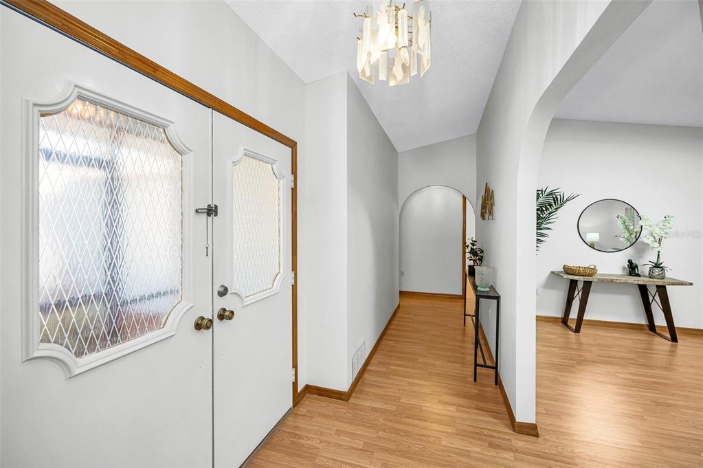 An entryway with light wood flooring, a white double door, and an arched hallway opening — 4745 SWALLOWTAIL DRIVE, NEW PORT RICHEY, FL