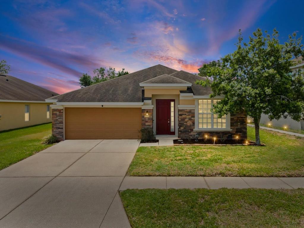 A single-story house with a tan garage, stone facade, and red front door at dusk — 13744 TRULL WAY, HUDSON, FL