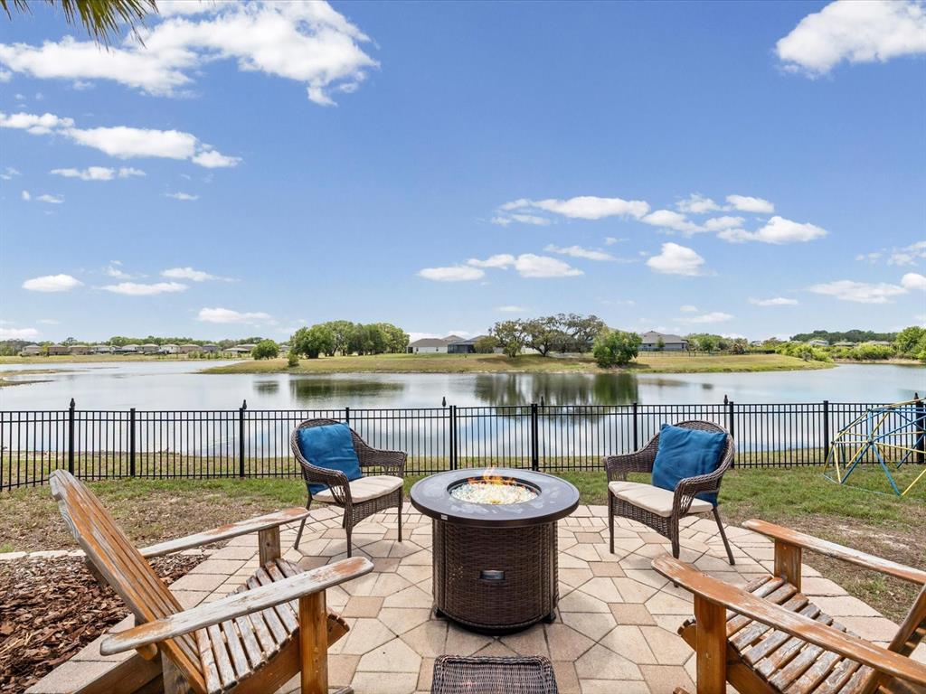 A patio with a fire pit and chairs overlooks a lake and a fenced yard — 13744 TRULL WAY, HUDSON, FL
