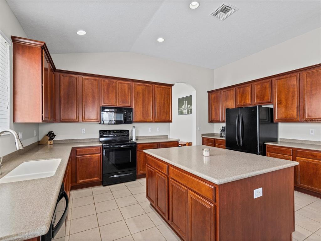 A kitchen with cherry wood cabinets, black appliances, and a central island with countertops — 13744 TRULL WAY, HUDSON, FL