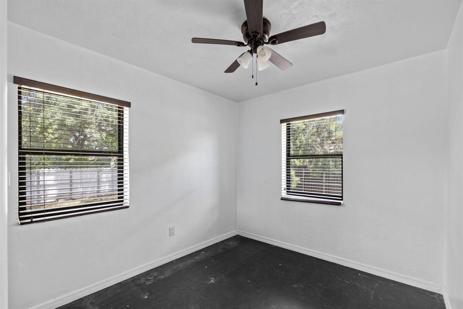 An empty bedroom with white walls, dark flooring, two windows with blinds, and a ceiling fan — 515 NW 88th Street, El Portal FL 33150, EL PORTAL, FL