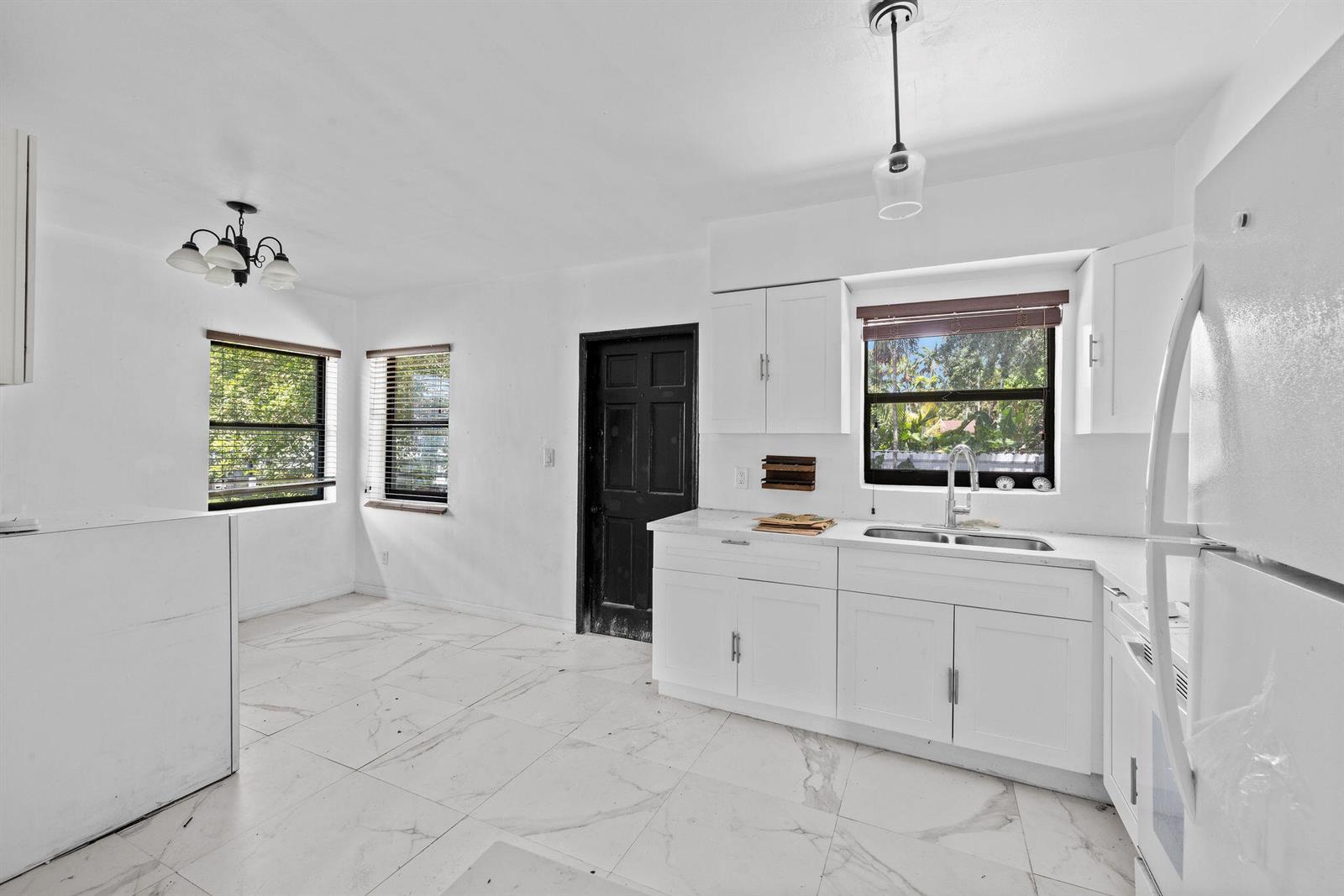 A white kitchen features marble-look tile floors, white cabinetry, a double sink, and two windows — 515 NW 88th Street, El Portal FL 33150, EL PORTAL, FL
