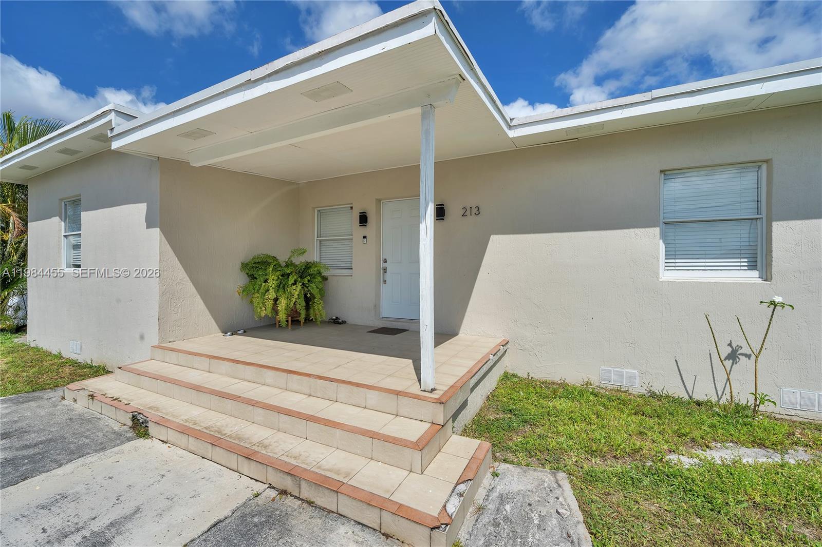 The exterior of a house features a tiled porch with steps and a white door — 213 W 20th St, Hialeah FL 33010, HIALEAH, FL