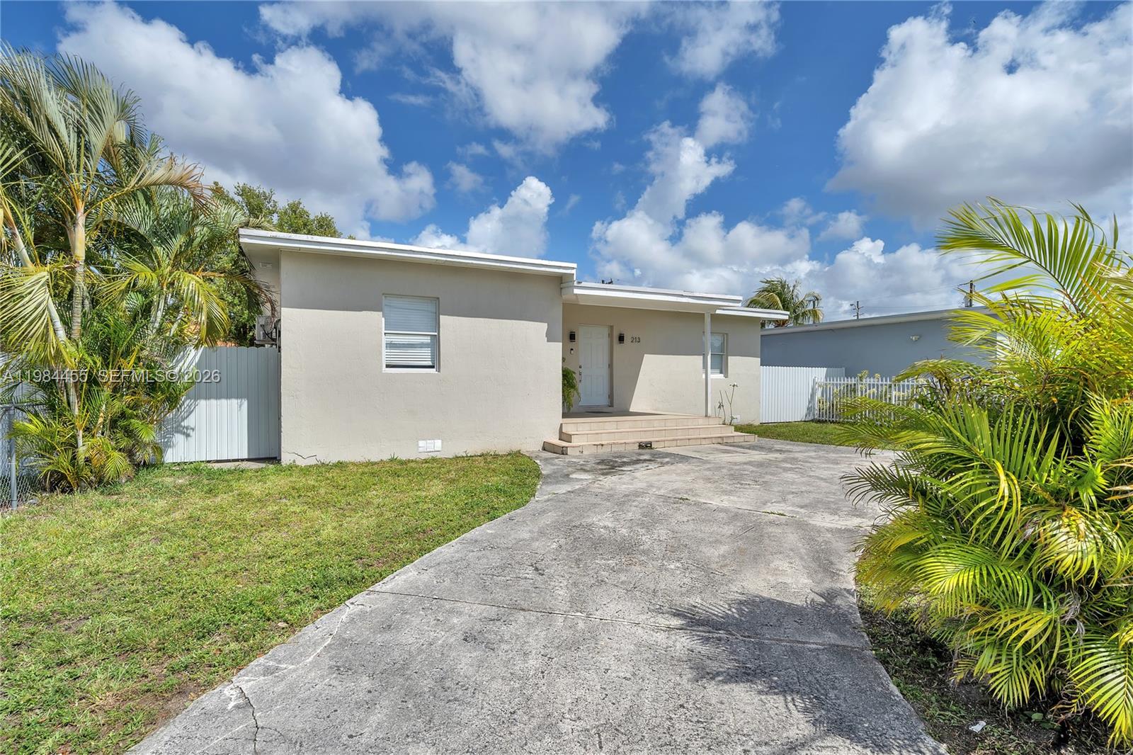 A single-story house with a concrete driveway, beige exterior, and palm trees in the yard — 213 W 20th St, Hialeah FL 33010, HIALEAH, FL