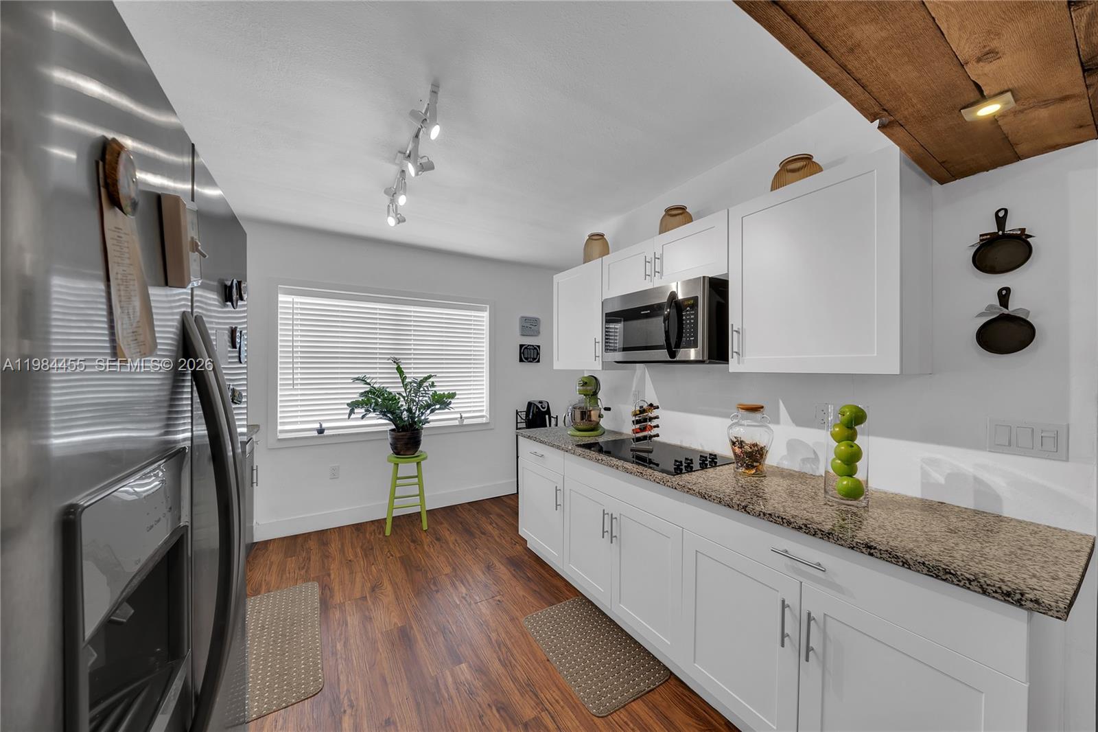 A kitchen features white cabinets, granite countertops, stainless steel appliances, and wood-look flooring — 213 W 20th St, Hialeah FL 33010, HIALEAH, FL