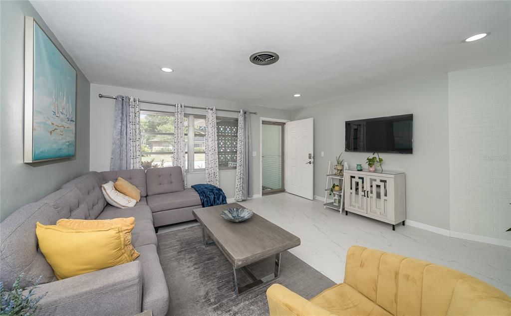 A living room features a gray sectional sofa, a yellow armchair, and a wall-mounted television — 2063 DUNSTON COVE ROAD, CLEARWATER, FL