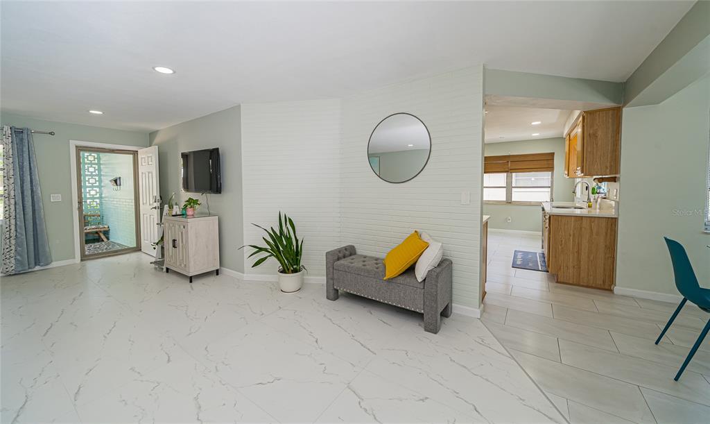 A living room with white marble-look tile floors, a white brick accent wall, and entryway — 2063 DUNSTON COVE ROAD, CLEARWATER, FL
