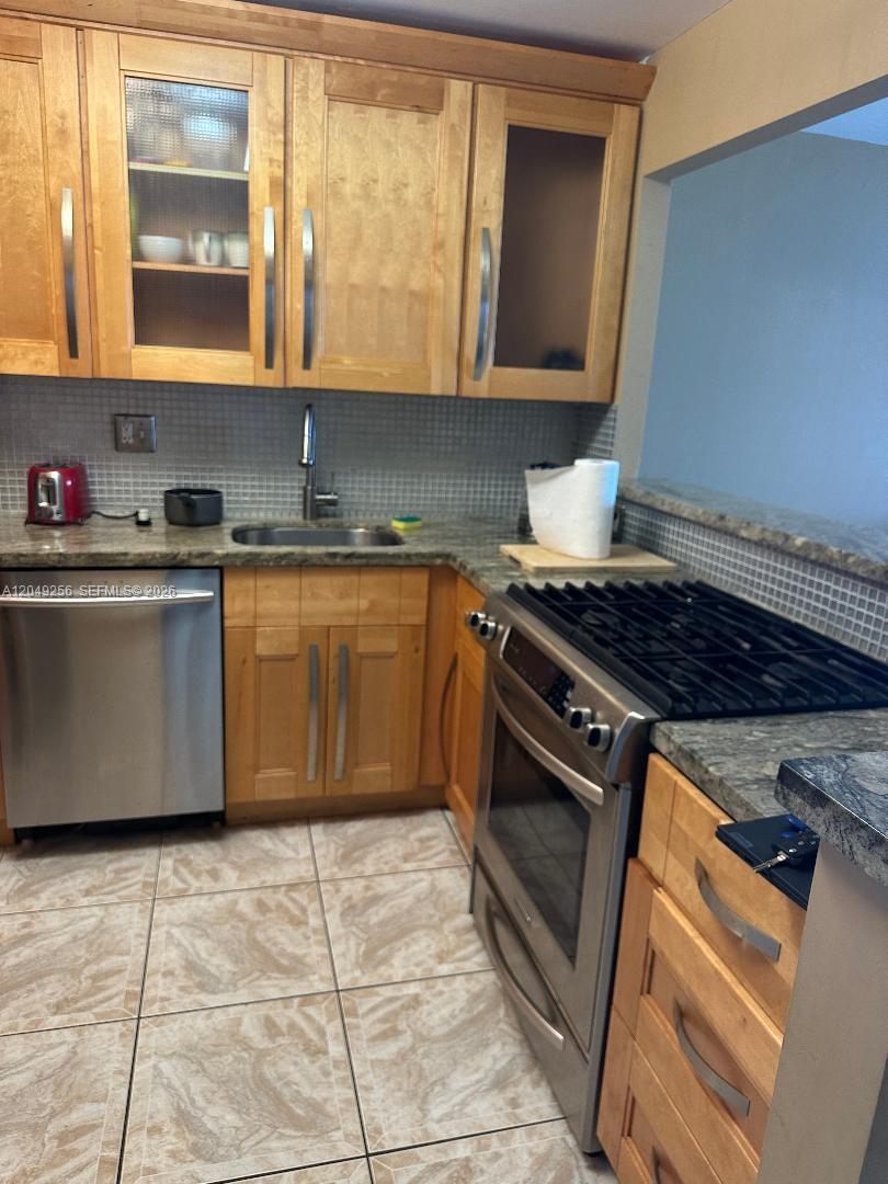 A kitchen features light wood cabinets, stainless steel appliances, and a gray tiled backsplash — 2030 S Ocean Dr # 416, Hallandale Beach FL 33009, HALLANDALE BEACH, FL