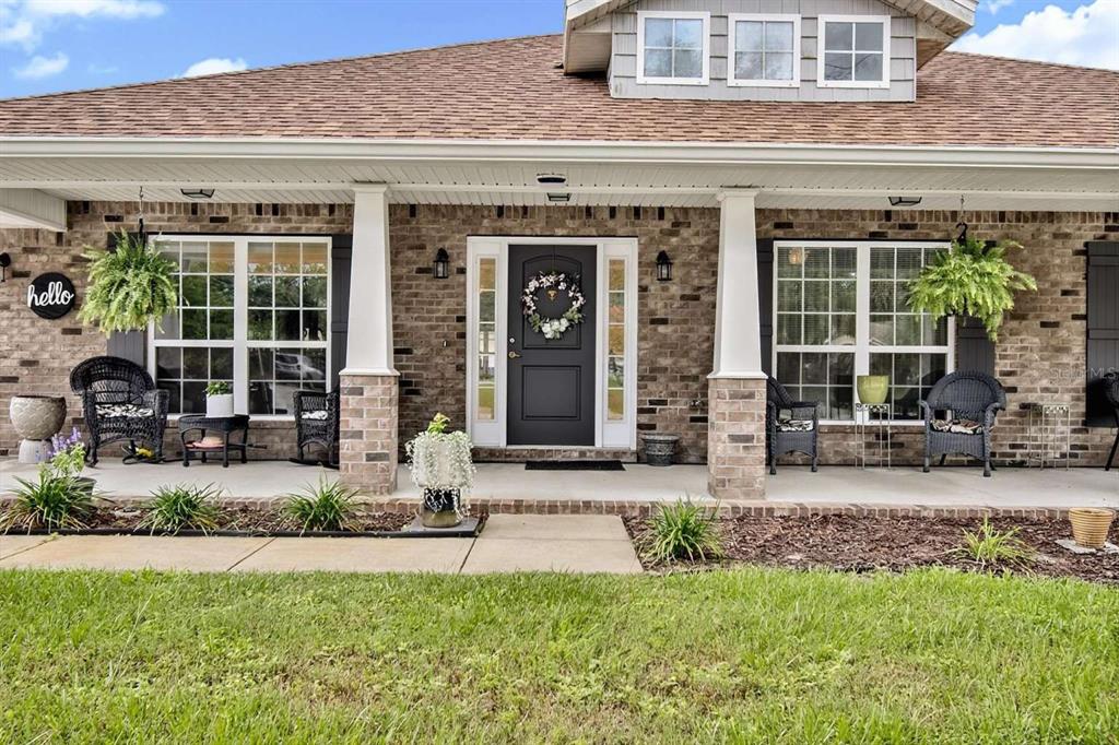 A brick house exterior features a covered front porch with white columns and black furniture — 16 WHITE STAR DRIVE, PALM COAST, FL