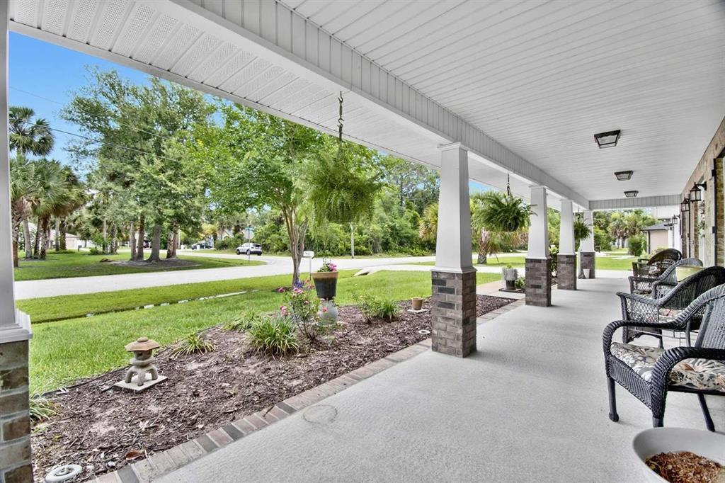 A covered front porch features stone-based columns, wicker chairs, and a view of the lawn — 16 WHITE STAR DRIVE, PALM COAST, FL