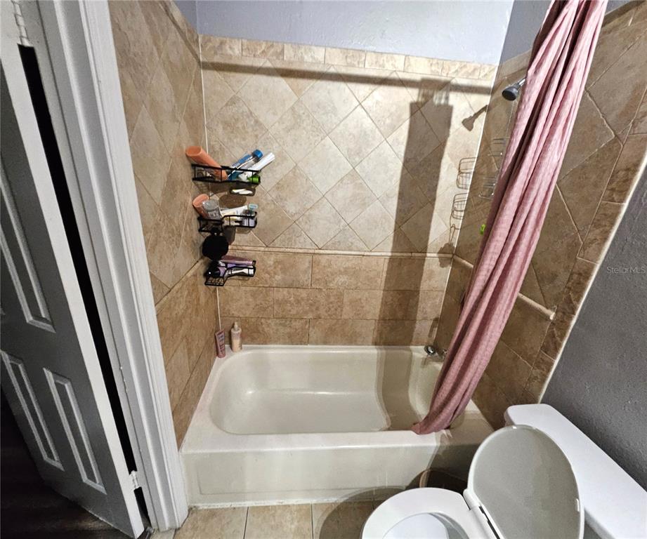 A bathroom features a beige tiled shower-tub combination with a hanging caddy and pink curtain — 4073 DIJON DRIVE UNIT 4073J, ORLANDO, FL