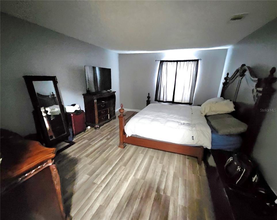 A bedroom features a wooden bed frame, a dresser with a television, and wood-look flooring — 4073 DIJON DRIVE UNIT 4073J, ORLANDO, FL