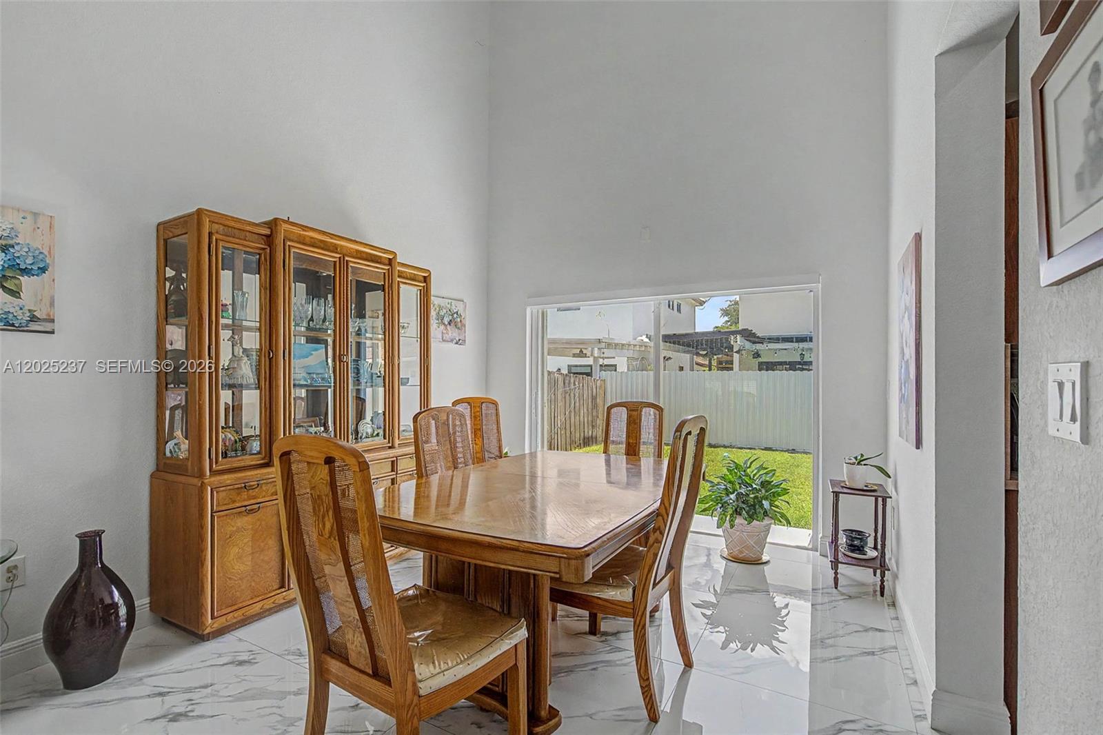 A dining room with a wooden hutch, table, chairs, and marble floors overlooks a backyard — 1551 SW 154th Ct, Miami FL 33194, MIAMI, FL