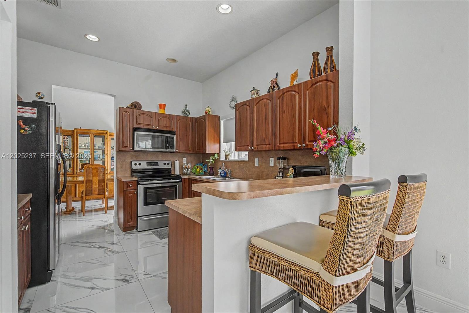 A kitchen features wood cabinets, stainless steel appliances, a breakfast bar, and white marble flooring — 1551 SW 154th Ct, Miami FL 33194, MIAMI, FL