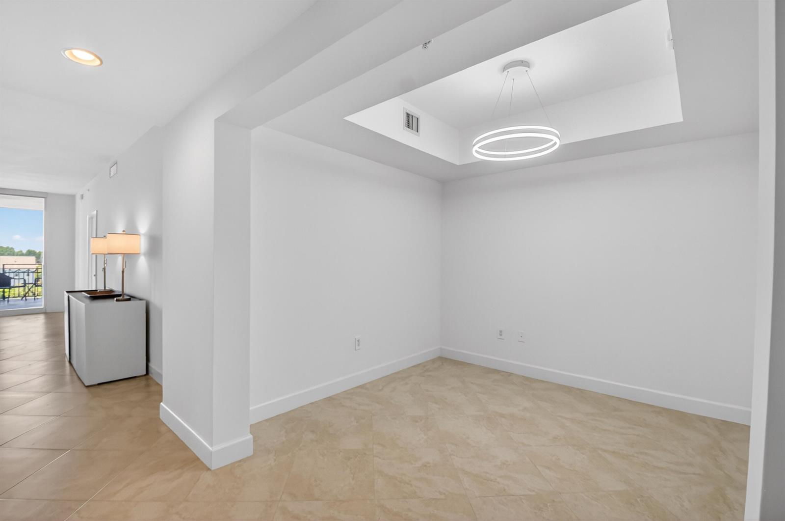 An empty room with a tray ceiling, modern ring chandelier, and light-colored tile flooring — 550 Okeechobee Boulevard # 423, West Palm Beach FL 33401, WEST PALM BEACH, FL