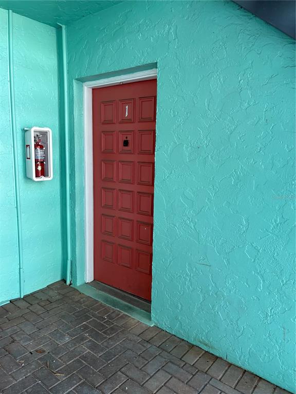 A red door labeled with the number one is set into a textured teal wall — 555 69TH AVENUE UNIT 1, ST PETERSBURG, FL