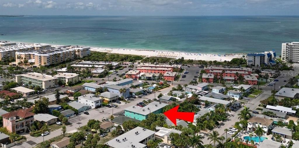 An aerial view shows a teal apartment building highlighted by a red arrow near the beach — 555 69TH AVENUE UNIT 1, ST PETERSBURG, FL