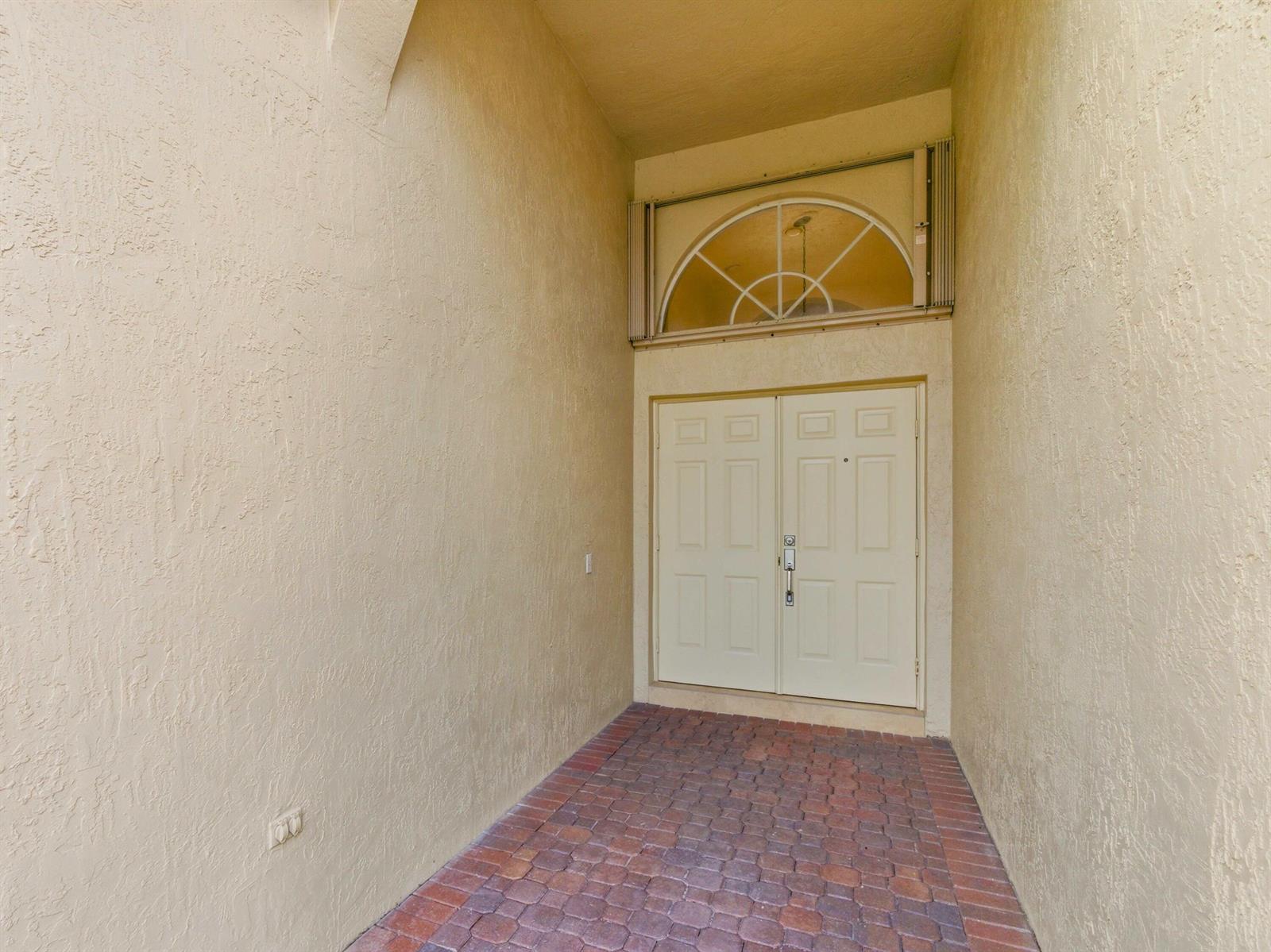 A recessed entryway features a brick floor, beige stucco walls, and a double front door — 10740 Grande Palladium Way, Boynton Beach FL 33436, BOYNTON BEACH, FL