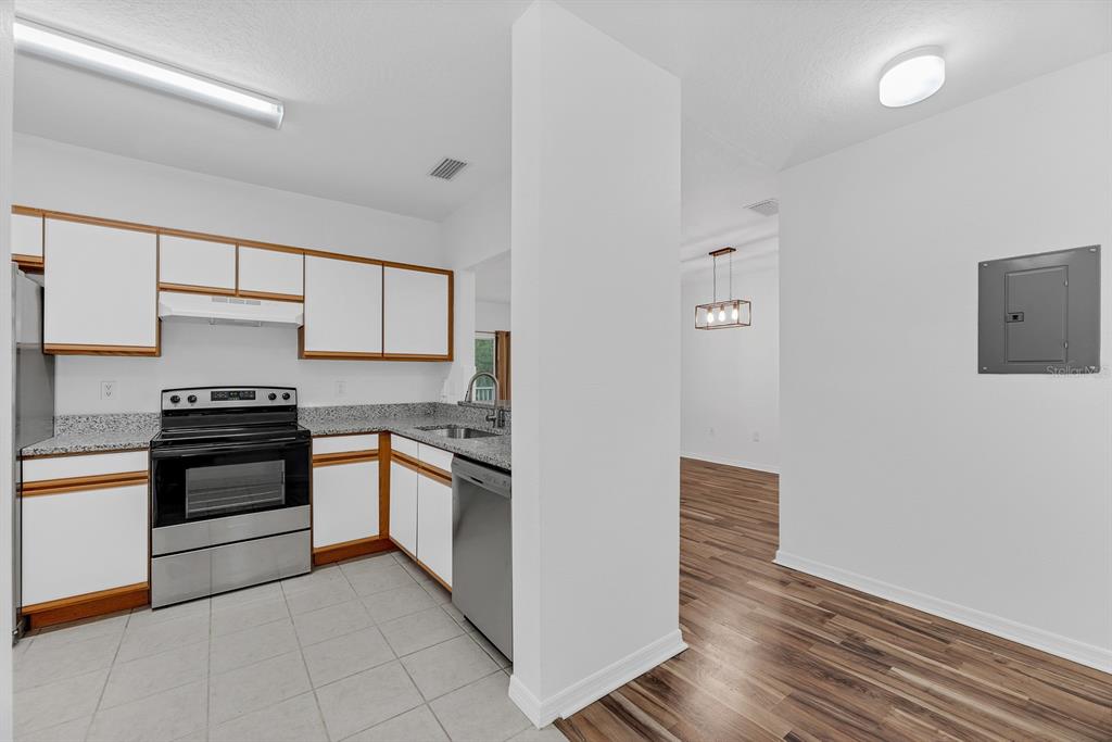 A kitchen with white cabinets, stainless steel appliances, and granite countertops next to a hallway — 6014 PORTSDALE PLACE UNIT 202, RIVERVIEW, FL