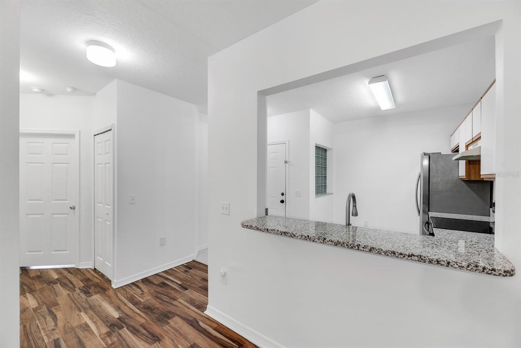 A view of a kitchen pass-through window with granite countertops and wood-look flooring — 6014 PORTSDALE PLACE UNIT 202, RIVERVIEW, FL