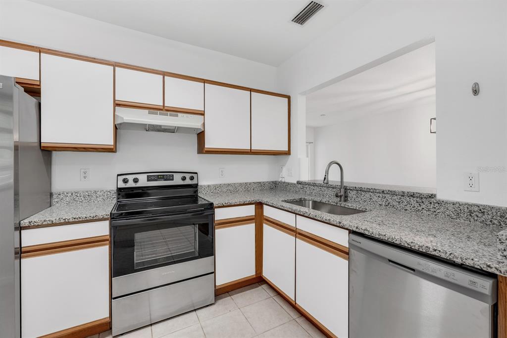 A kitchen with white cabinets, wood trim, granite countertops, and stainless steel appliances — 6014 PORTSDALE PLACE UNIT 202, RIVERVIEW, FL