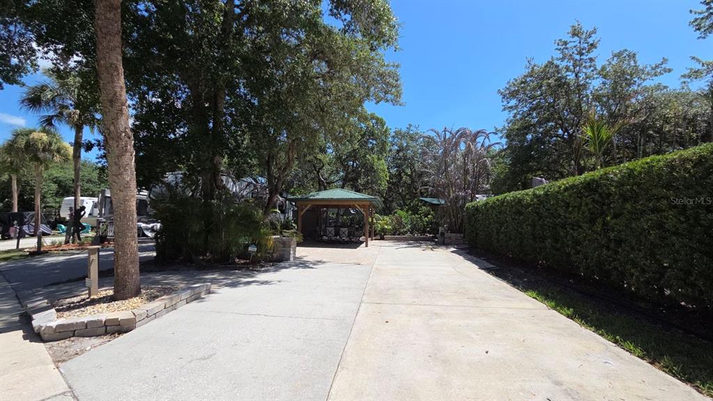 A concrete driveway leads to a covered gazebo surrounded by trees and a tall hedge — 234 STALLION LANE, RIVER RANCH, FL