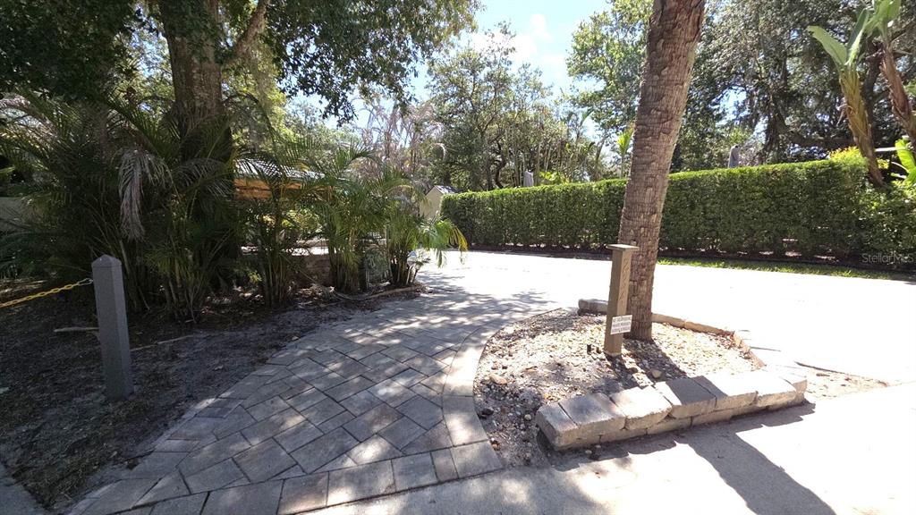 A paved walkway leads toward a shaded patio area surrounded by trees and a hedge — 234 STALLION LANE, RIVER RANCH, FL