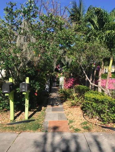 A paved walkway leads through lush greenery toward a gated entrance with two mailboxes — 12 S Ocean Breeze # 2, FL 33460, FL