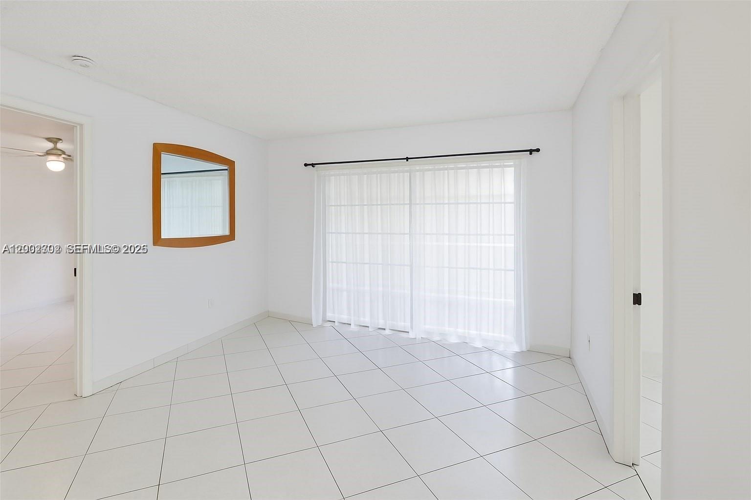 A bright, empty room features white walls, white tiled floors, a mirror, and sliding glass doors — 2600 Collins Ave # 405, Miami Beach FL 33140, MIAMI BEACH, FL