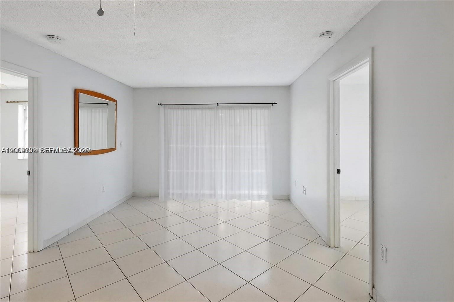 An empty room features white walls, light-colored tile flooring, and a large sliding glass door — 2600 Collins Ave # 405, Miami Beach FL 33140, MIAMI BEACH, FL