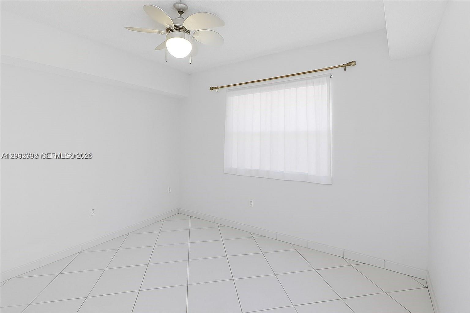 An empty bedroom features white walls, white tile flooring, and a ceiling fan — 2600 Collins Ave # 405, Miami Beach FL 33140, MIAMI BEACH, FL