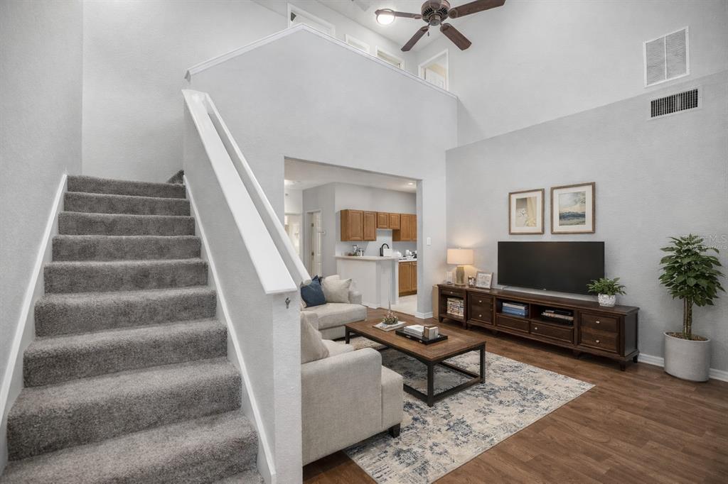 A living room with gray carpeted stairs, a vaulted ceiling, and a view into the kitchen — 231 NE 28TH AVENUE UNIT 103, OCALA, FL