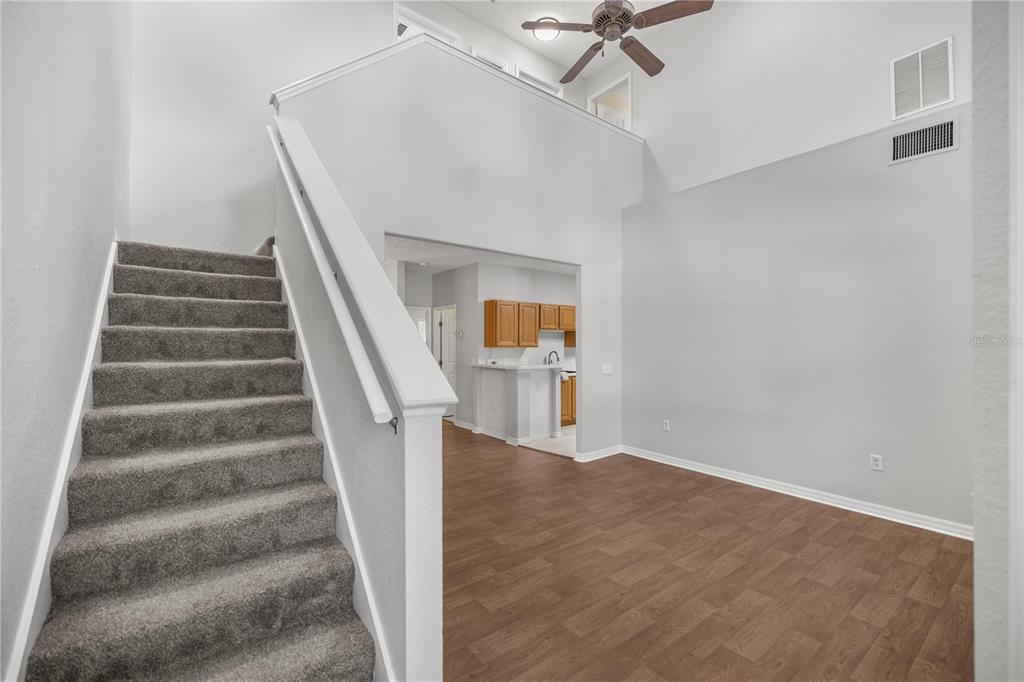 A carpeted staircase leads up beside a living area with wood-look flooring and high ceilings — 231 NE 28TH AVENUE UNIT 103, OCALA, FL