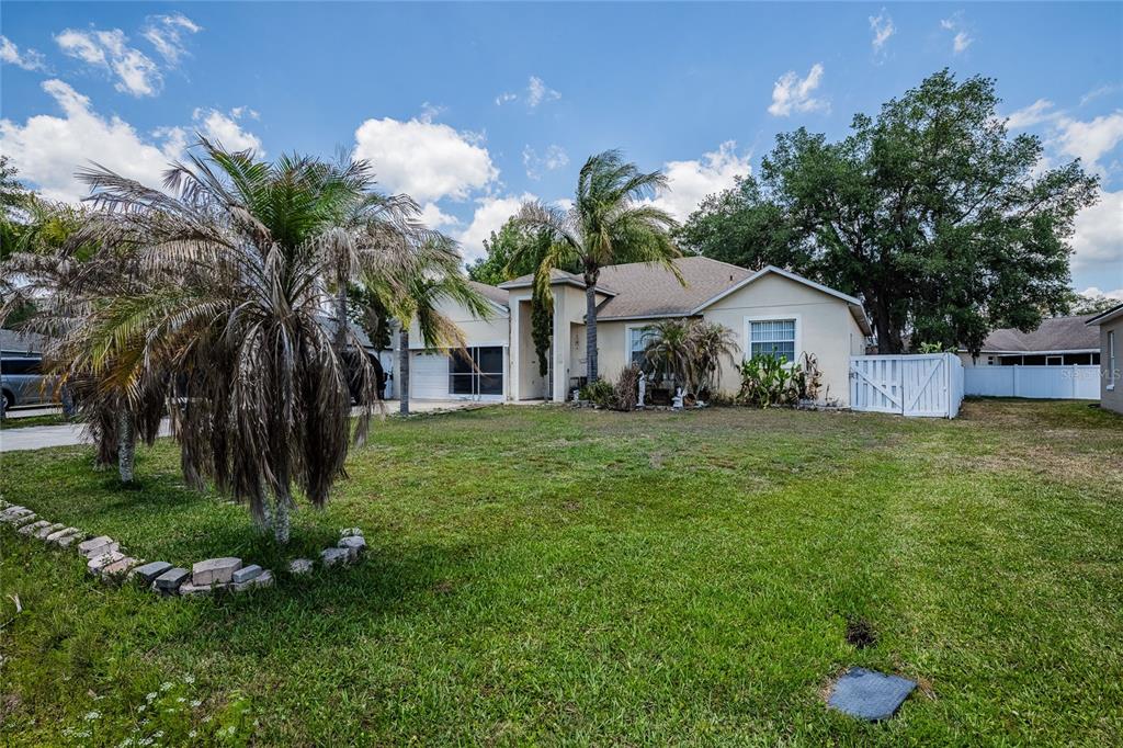 A single-story house with a tan exterior, a palm tree, and a white fence — 427 LARK COURT, KISSIMMEE, FL