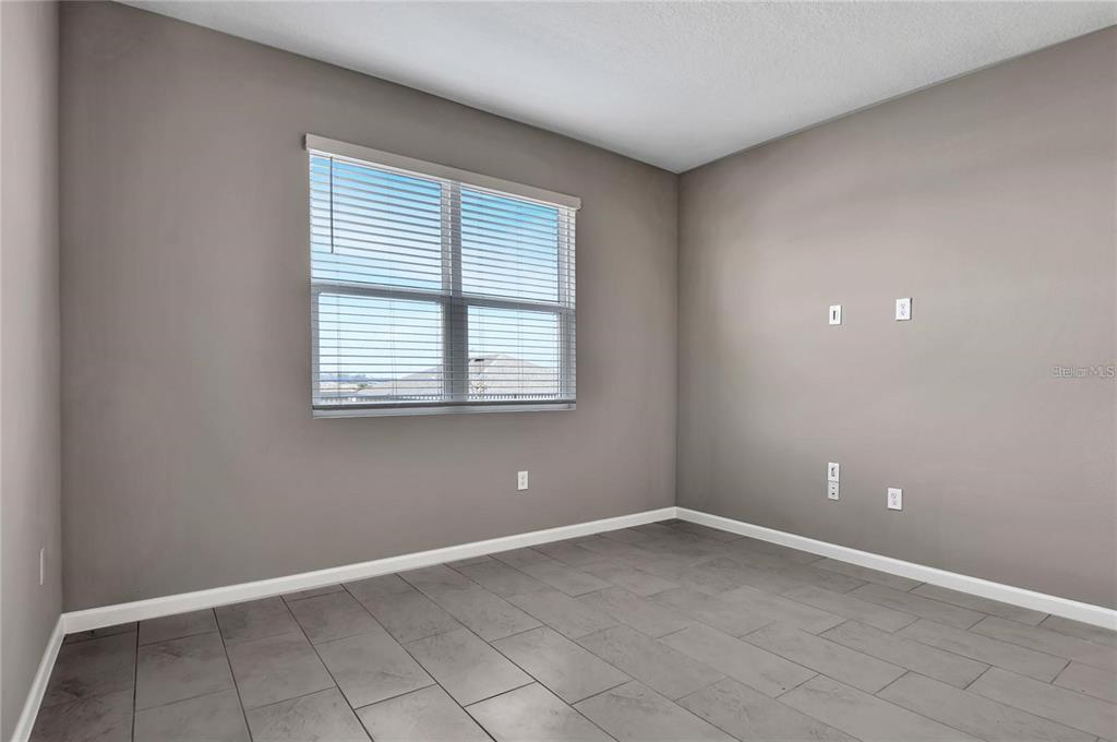 An empty room features gray walls, a window with blinds, and gray tile flooring — 830 BALLANTYNE DRIVE, LAKE WALES, FL