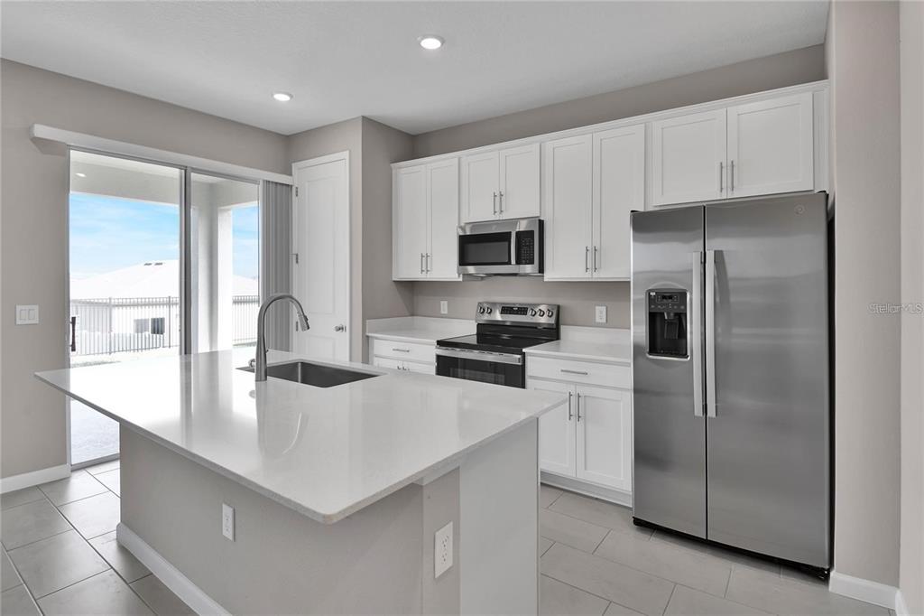 A modern kitchen features white cabinets, stainless steel appliances, a quartz island, and tile flooring — 830 BALLANTYNE DRIVE, LAKE WALES, FL