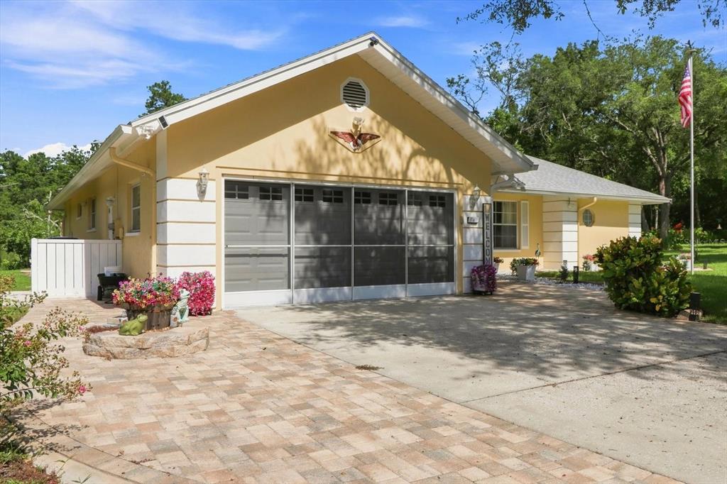 A yellow house with a screened-in garage, a paved driveway, and an American flag — 6 DUSTY MILLER COURT, HOMOSASSA, FL