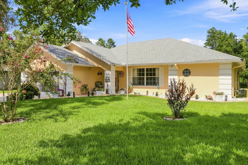A single-story yellow house with a gray roof and an American flag in the yard — 6 DUSTY MILLER COURT, HOMOSASSA, FL