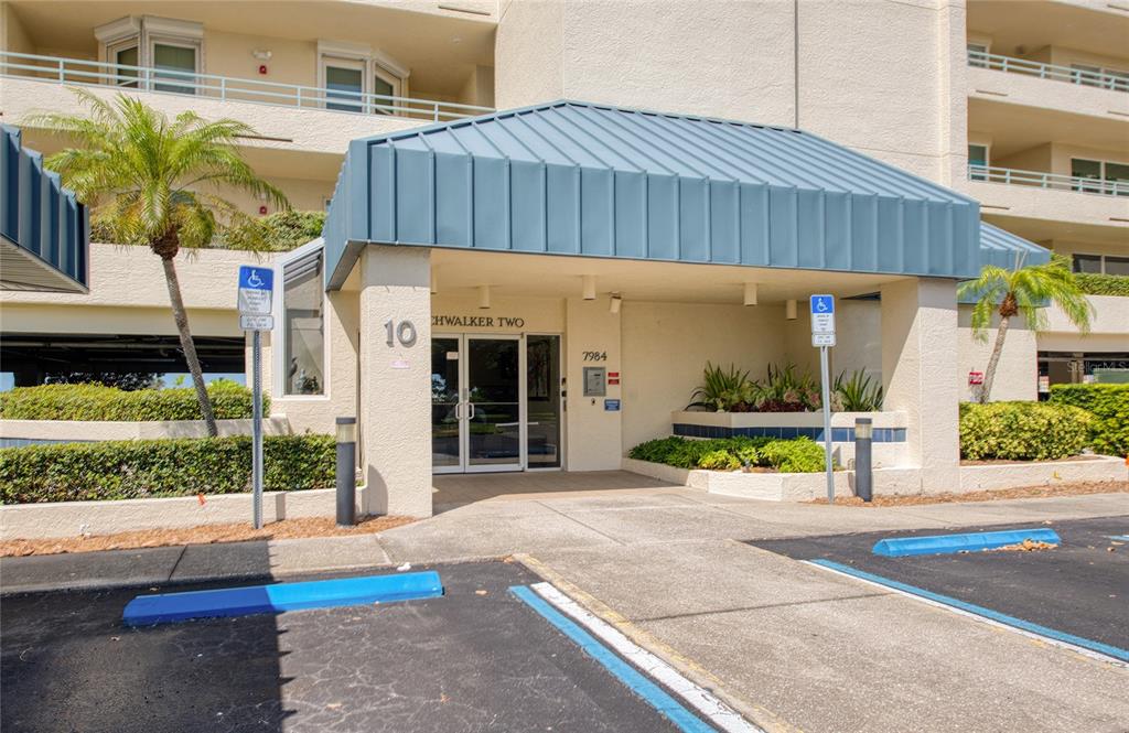 The exterior entrance of a multi-story residential building features a blue metal awning — 7984 SAILBOAT KEY BOULEVARD S UNIT 303, ST PETERSBURG, FL
