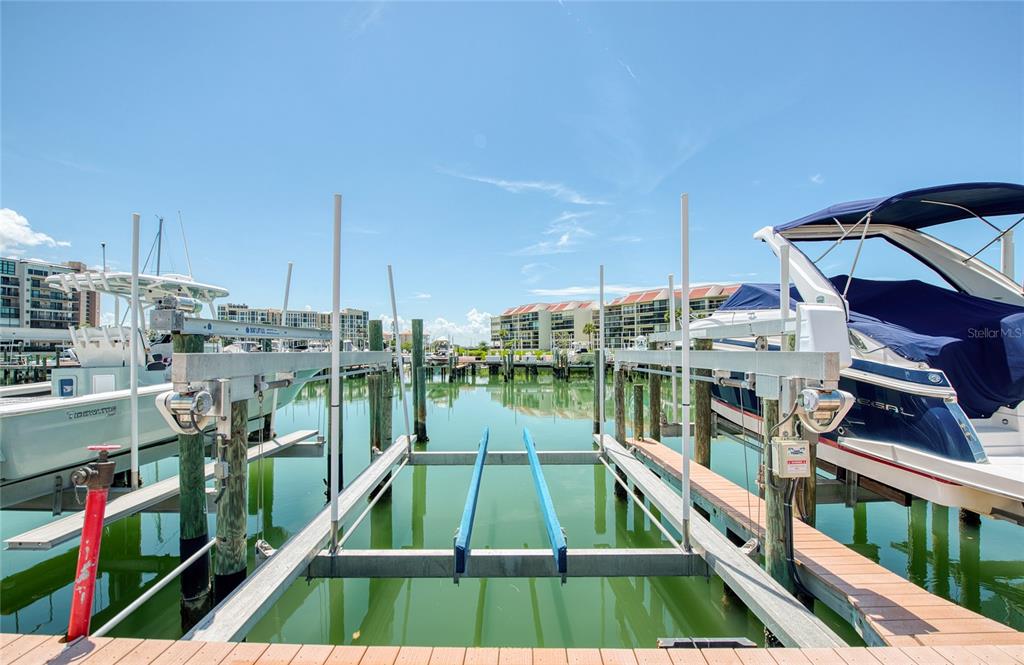 A boat lift sits between two docked boats in a marina with buildings in the background — 7984 SAILBOAT KEY BOULEVARD S UNIT 303, ST PETERSBURG, FL