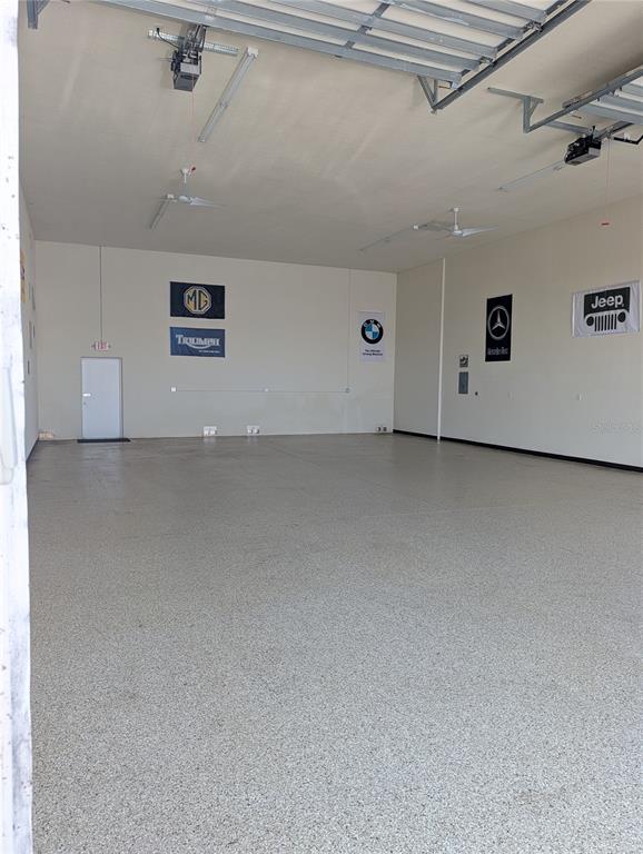 A spacious, empty garage features a speckled epoxy floor, white walls, and several automotive banners — 8290 BURNT STORE ROAD UNIT B5 and B6, PUNTA GORDA, FL