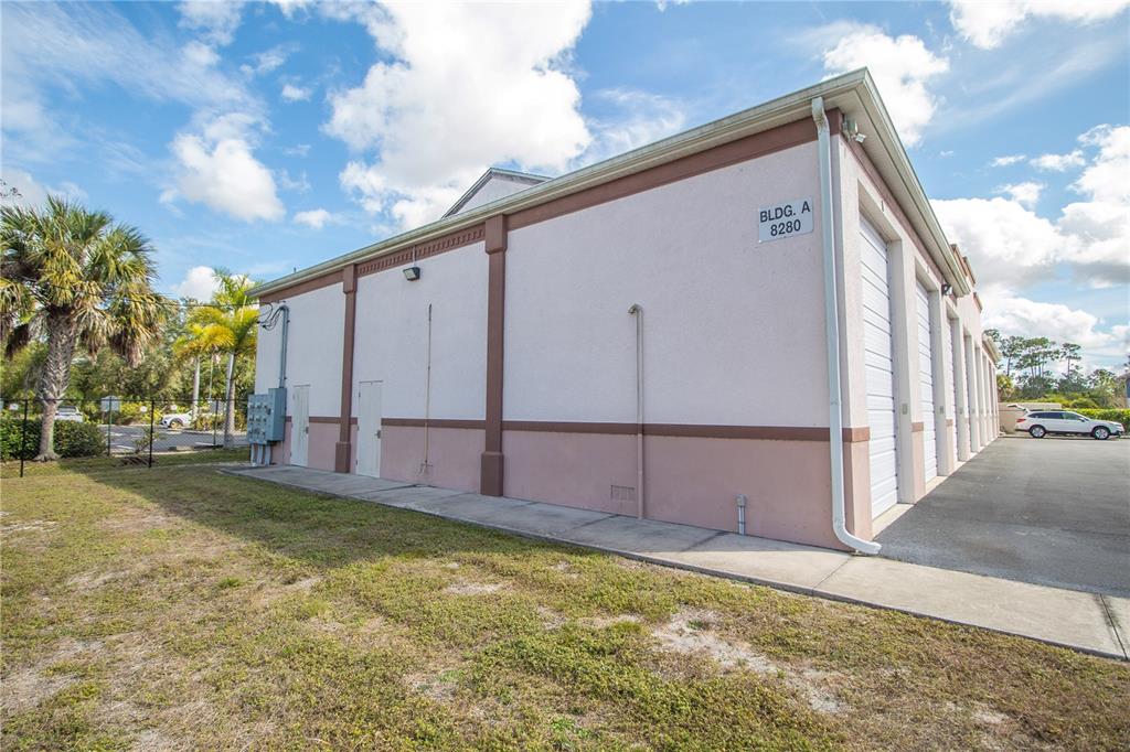 The exterior of a light-colored commercial building features multiple roll-up garage doors and a sidewalk — 8290 BURNT STORE ROAD UNIT B5 and B6, PUNTA GORDA, FL