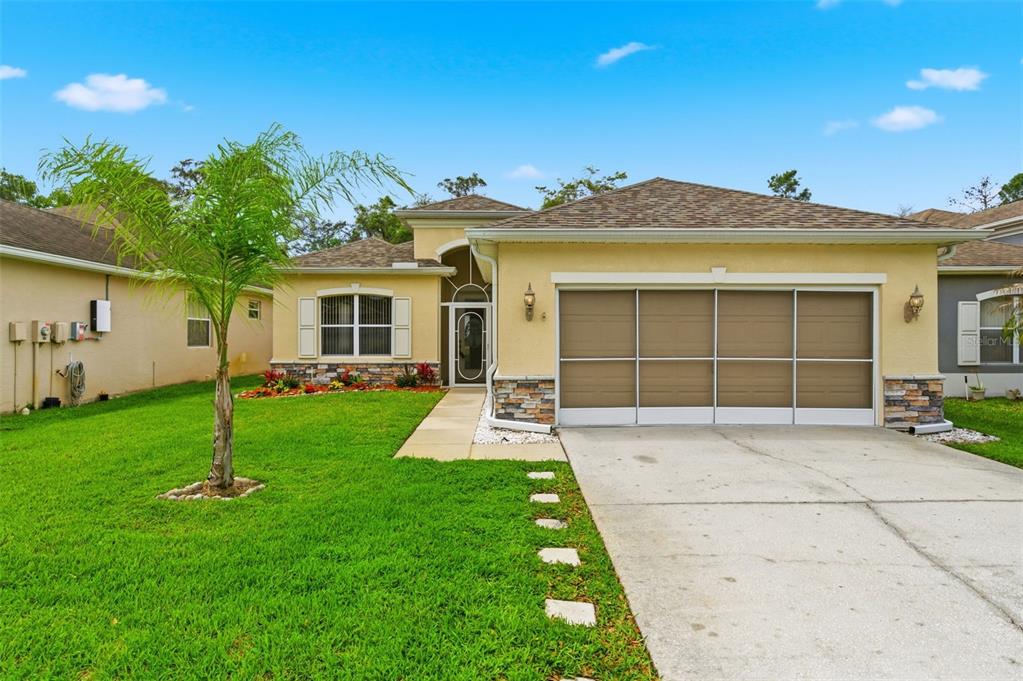 A single-story house with a tan stucco exterior, a two-car garage, and a front lawn — 14753 POTTERTON CIRCLE, HUDSON, FL