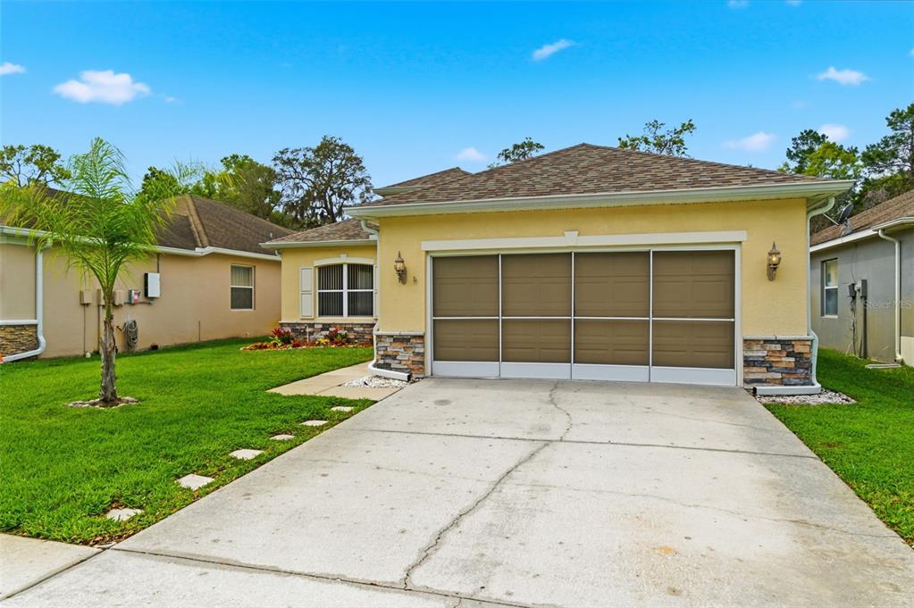 A yellow single-story house with a stone-accented facade and a multi-panel garage door — 14753 POTTERTON CIRCLE, HUDSON, FL