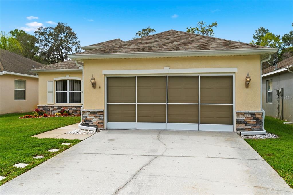 A single-story house exterior features a tan stucco facade, stone accents, and a sliding garage screen — 14753 POTTERTON CIRCLE, HUDSON, FL