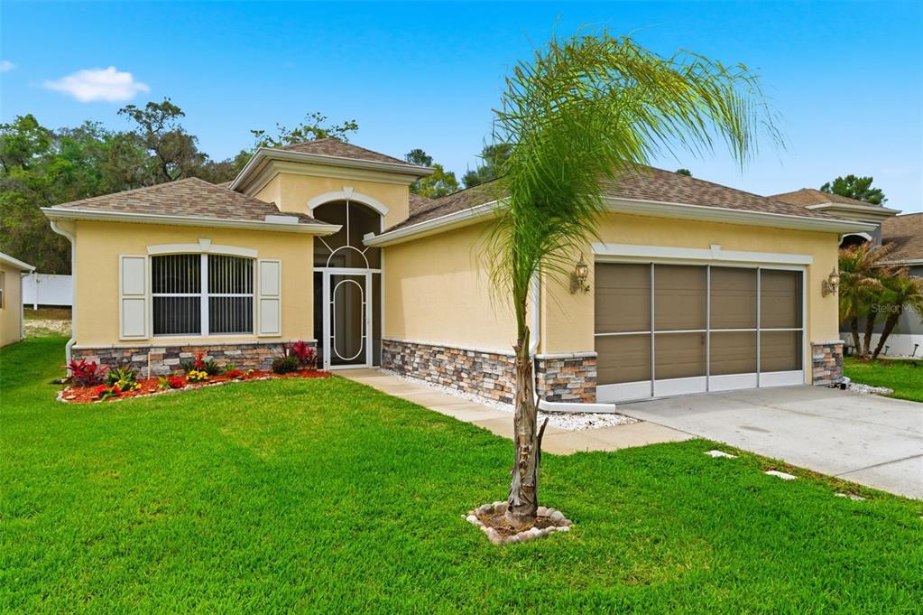 A single-story house with a yellow stucco exterior, stone accents, and a two-car garage — 14753 POTTERTON CIRCLE, HUDSON, FL