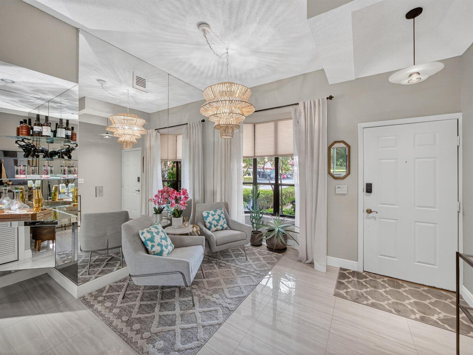 A bright entryway features two gray armchairs, a large wall mirror, and a tiered chandelier — 7472 La Paz Boulevard # 109, Boca Raton FL 33433, BOCA RATON, FL