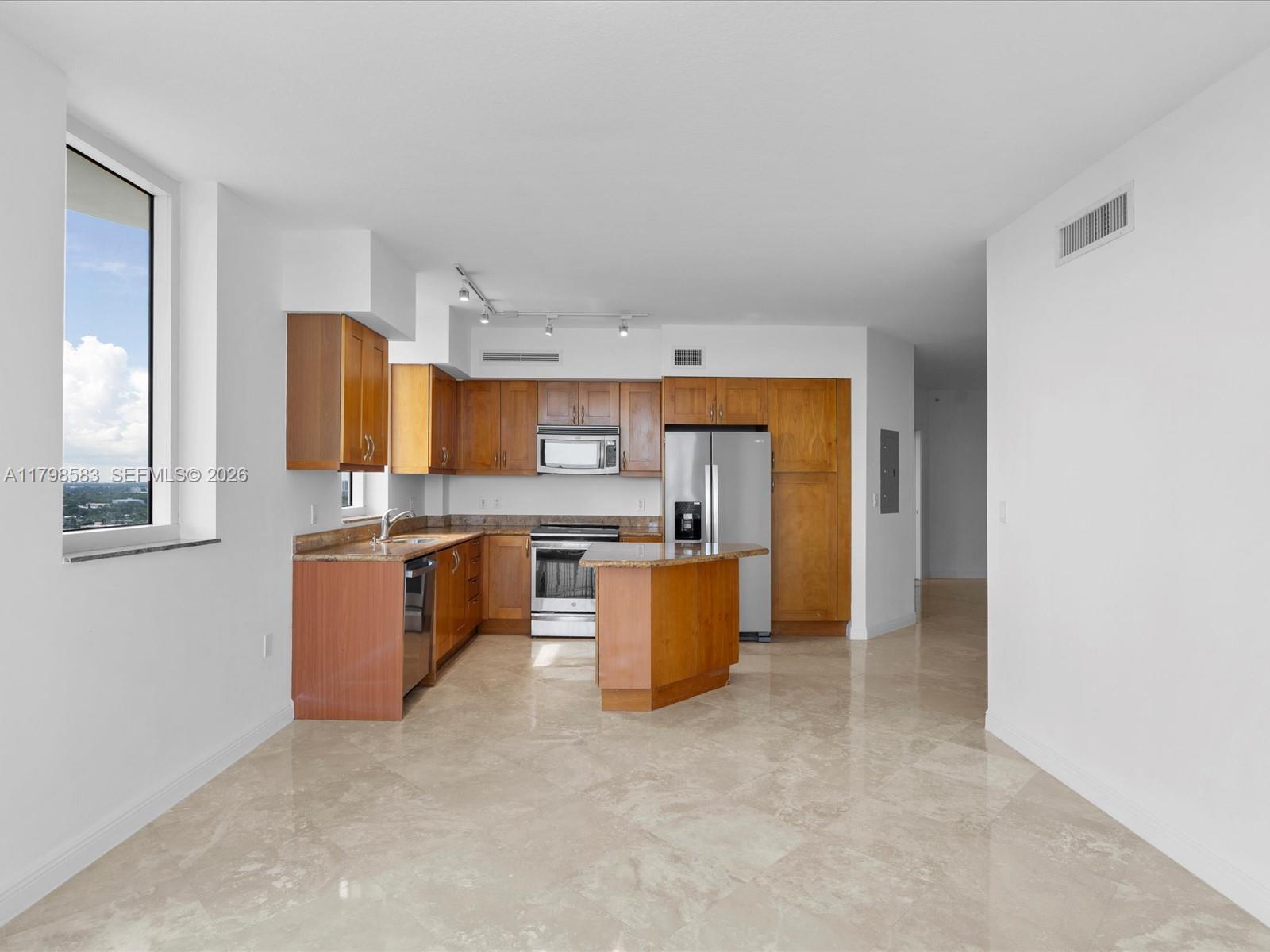 A kitchen features wooden cabinets, granite countertops, stainless steel appliances, and light-colored tile flooring — 1745 E Hallandale Beach Blvd # 2007W, Hallandale Beach FL 33009, HALLANDALE BEACH, FL